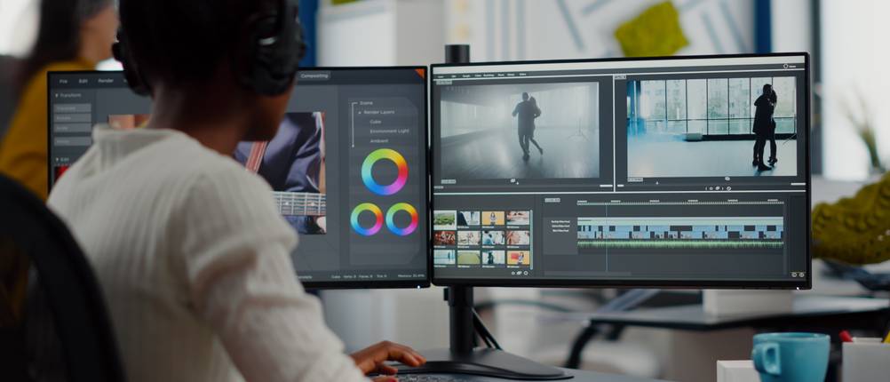 Videobearbeitungsprogramme im Test: Ein junger Mann sitzt vor mehreren Bildschirmen und bearbeitet ein Video.