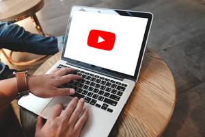 Videobearbeitungsprogramme im Test: Eine Person bedient einen Laptop, auf dessen Bildschirm das YouTube-Logo zu sehen ist.