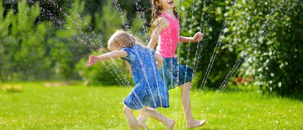 zwei Kinder spielen an einem Viereckregner