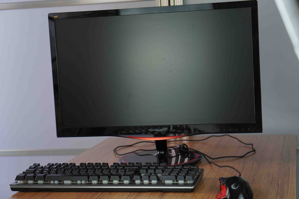 Gesamtansicht von vorn eines schwarzen 144-Hz-Monitors im Test. Im Vordergrund eine schwarze Tastatur und Maus, die auf einem Holztisch stehen.