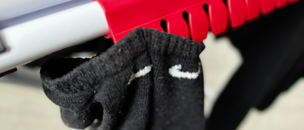 Nahaufnahme der Kleinteilehalterung des Vileda Doble. Eine schwarze Socke ist ohne Klammer in einem der roten Haken eingehängt.