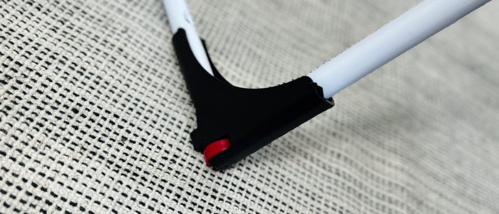 Detailansicht des schwarzen Rollenfußes vom Vileda Doble. Das rote Radelement ist auf einem hellen Teppich zu sehen.