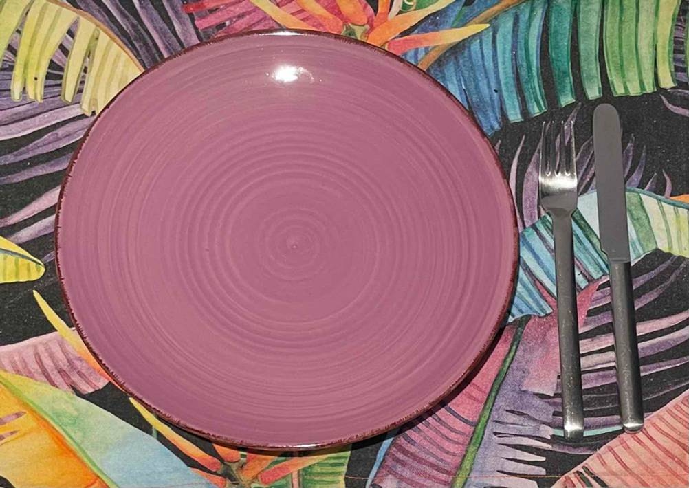 Im Test: Geschirr, bestehend aus einem weinroten Teller neben Gabel und Messer von oben gesehen auf einer bunt gemusterten Tischdecke.
