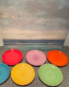 Geschirr im Test: mehrere bunte Teller von Villa Deste Home stehen nebeneinander vor einem mediterranen Bild.