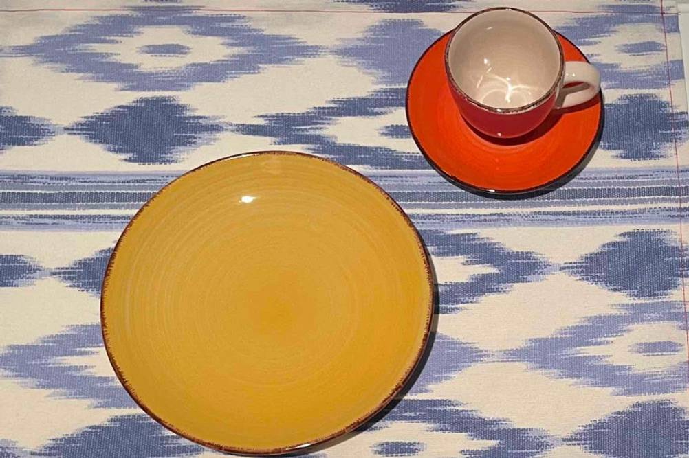 Geschirr im Test: Teller und Tasse mit Untertasse in gelb und orange stehen auf blau-weiß gemusterter Fläche.