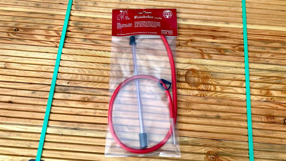 Ein getesteter Weinheber liegt in transparenter Originalverpackung auf einer Holzfläche.
