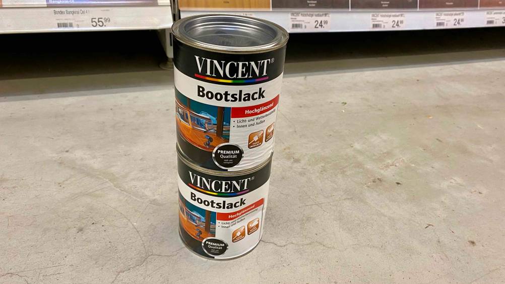 Im Test: Zwei Dosen Bootslack übereinandergestapelt vor einem Regal auf einem Betonboden.