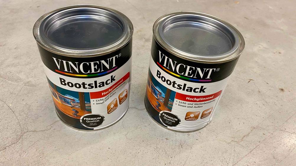 Bootslack getestet: Zwei Dosen von schräg oben nebeneinander auf einem Betonboden stehend.
