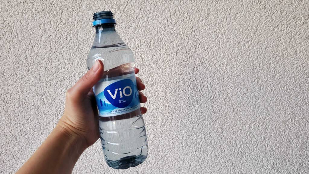 Eine 500-ml-Kunststoffflasche mit stillem Mineralwasser im Test in einer Damenhand vor weißer Wand.