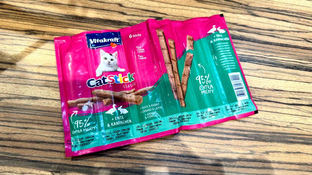 Eine 6er Packung getestete Katzensticks liegt auf einer Holzfläche.