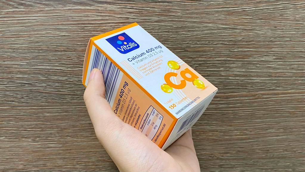 Im Test: Hand hält eine Verpackung mit Vitalis Calcium 400 mg vor Holzfläche.