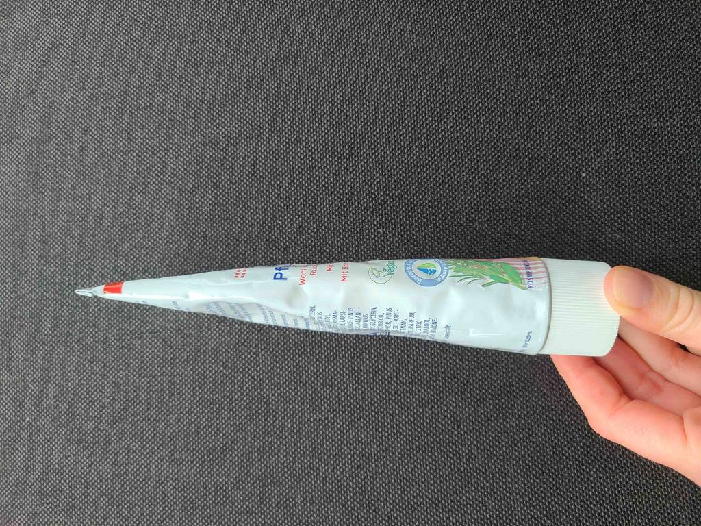 Eine Hand hält die Tube mit der getesteten Wärmesalbe über einer schwarzen Oberfläche.