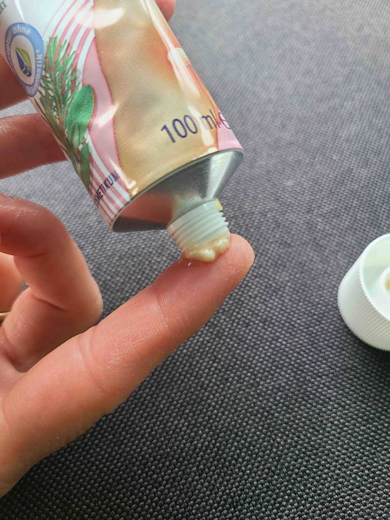 Die getestete Wärmesalbe in der 100-ml-Tube kommt auf einer Fingerspitze vor einer schwarzen Oberfläche.