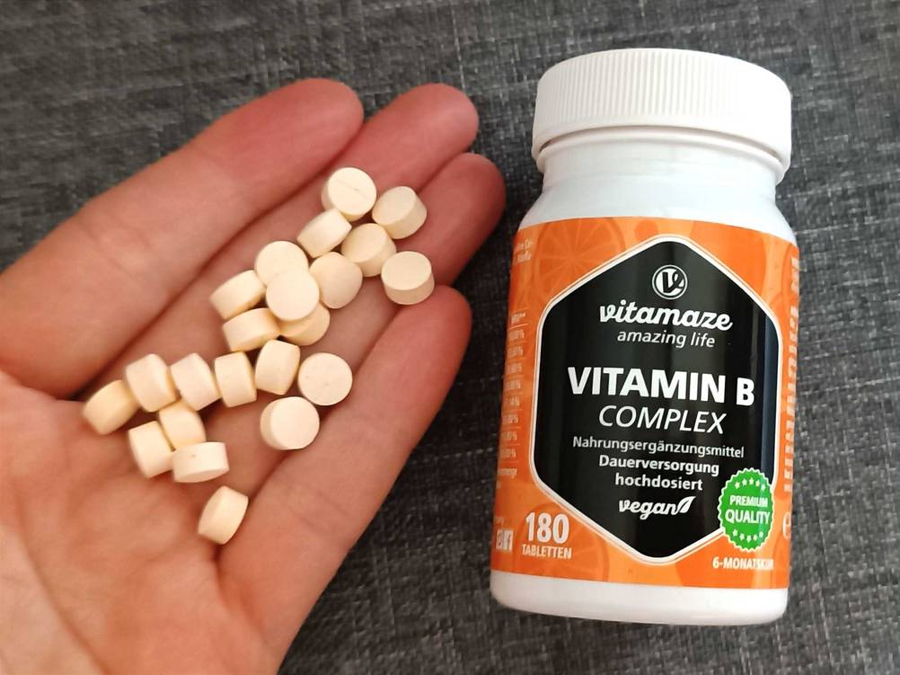 Neben einer Dose des Vitamin-B-Komplex im Test befindet sich eine Hand mit den Tabletten.