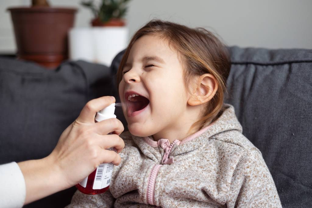 Vitamin-b12-Spray-test: Eine Frau sprüht mit einem Mundspray in den Mund eines Kindes.