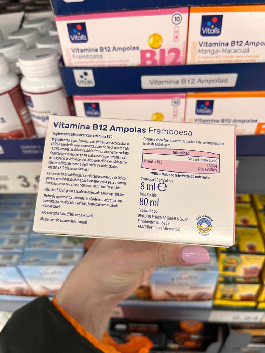Eine Hand hält die Rückseite einer Verpackung des getesteten Vitamin B12 vor ein Regal.