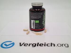 vitamin-c-test: Eine dunkle Dose mit Kapseln und offene und geschlossene Kapseln liegen auf einem Tisch hinter einem Vergleich.org-Logo. 