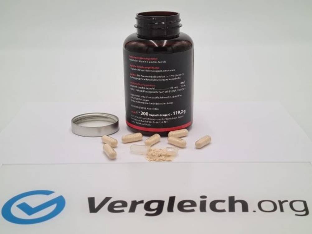 vitamin-c-test: Eine offene Dose und Kapseln liegen auf einem Tisch hinter einem Vergleich.org-Logo.