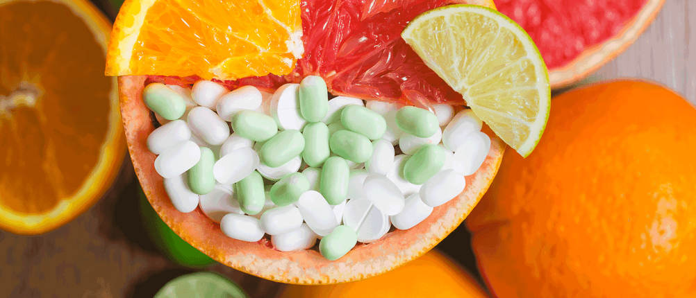 vitamin-c-test: Auf einem Tisch liegen aufgeschnittene Orangen und Grapefruit. Auf einer Grapefruit liegen mehrere Tabletten. 