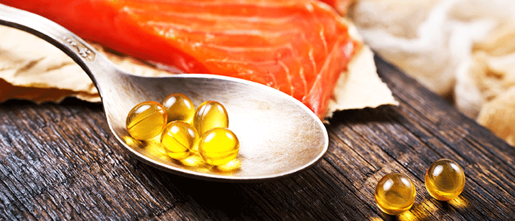 vitamin d tabletten auf einem löffel und im hintergrund lachsfilet