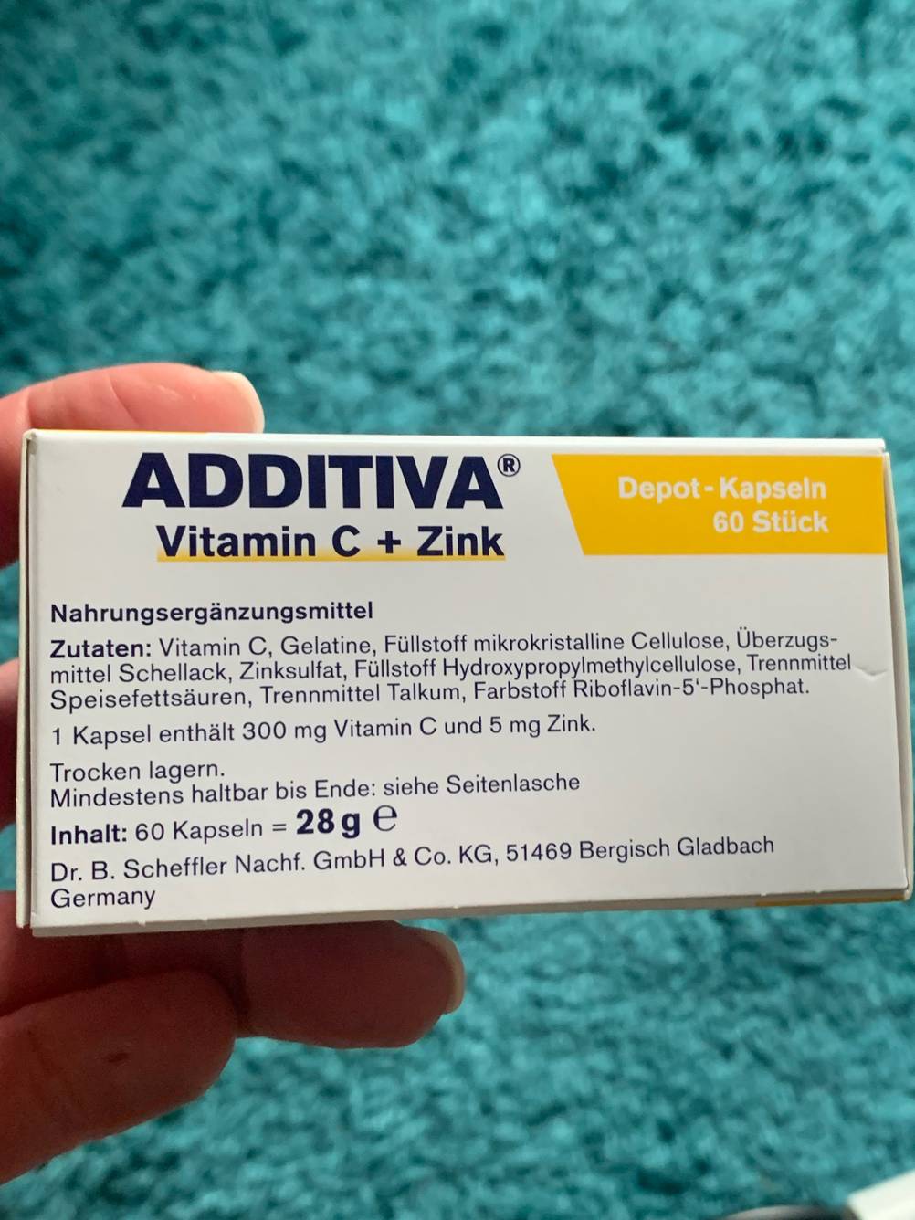 Eine Hand hält die Packung der getesteten Vitamin-Kapseln vor eine blaue Fläche.