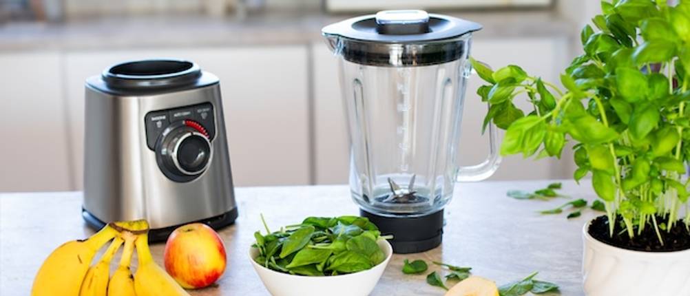 Vitamix-Mixer im Test: Ein Gehäuse eines Standmixers und ein Mixbehälter stehen mit Zutaten für einen Smoothie auf einer weißen Abstellfläche.