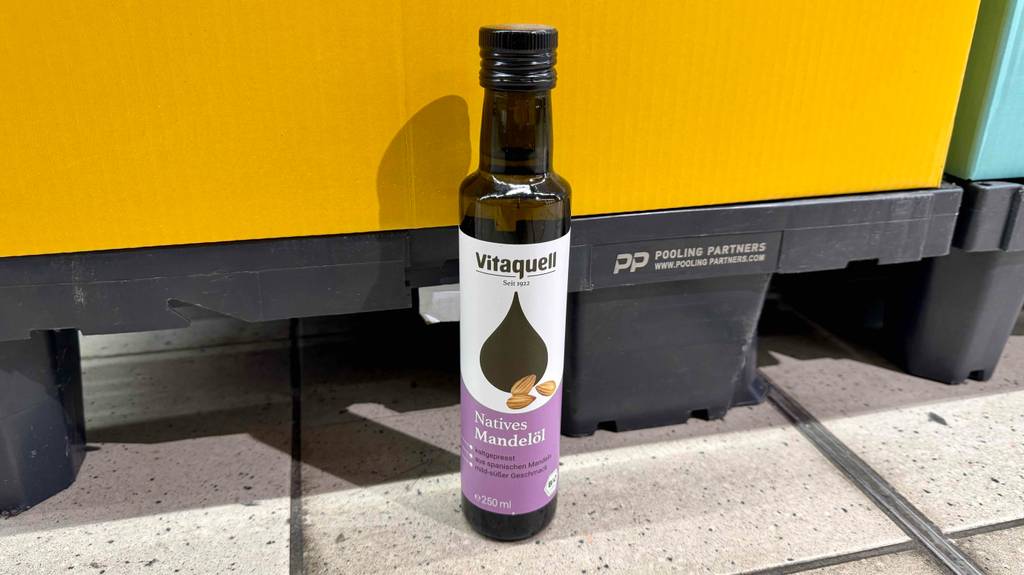 Eine 250-ml-Flasche mit getestetem Bio-Mandelöl steht auf dem Boden vor einem Regal.