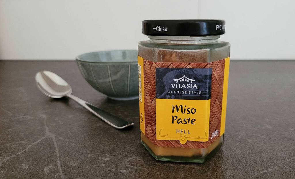 Miso Paste im Test: Ein Glas der Marke Vitasia Japanese steht auf einer schwarzen Arbeitsfläche, im Hintergrund ein Löffel und eine Schale.