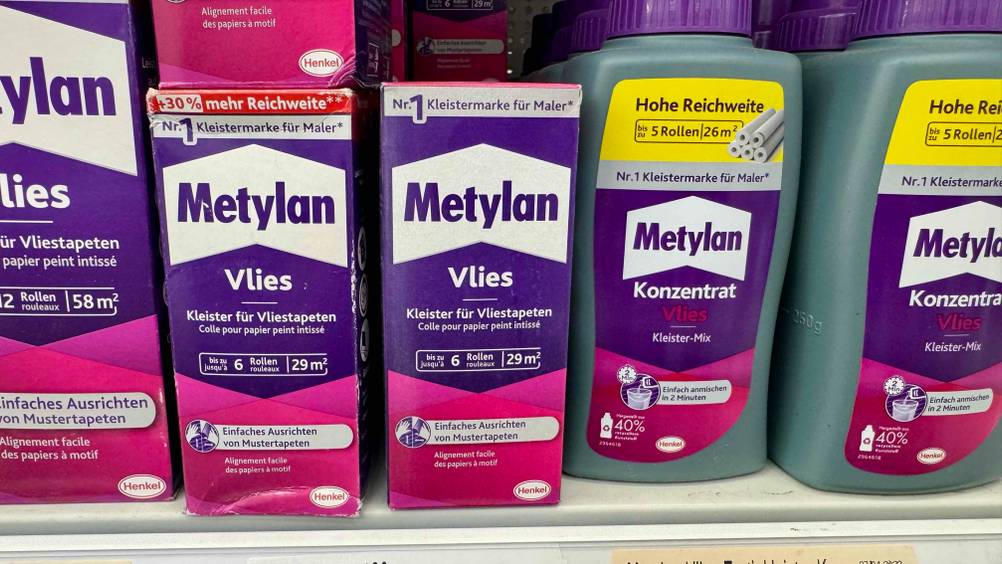 Mehrere Packung des getesteten Vliestapetenkleisters stehen neben anderen Produkten in einem Verkaufsregal.