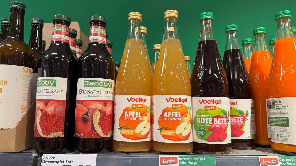 Getesteter Apfelsaft von Voelkel steht neben anderen Fruchtgetränken in Glasflaschen auf einem Verkaufsregal.