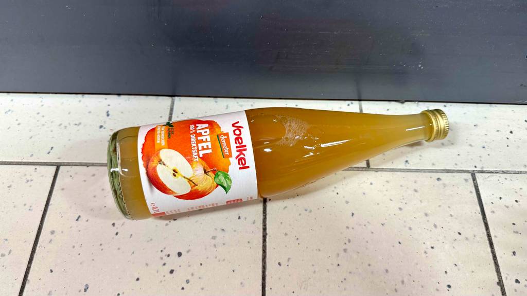 Ein getesteter Apfelsaft in der Glasflasche liegt auf dem Boden.