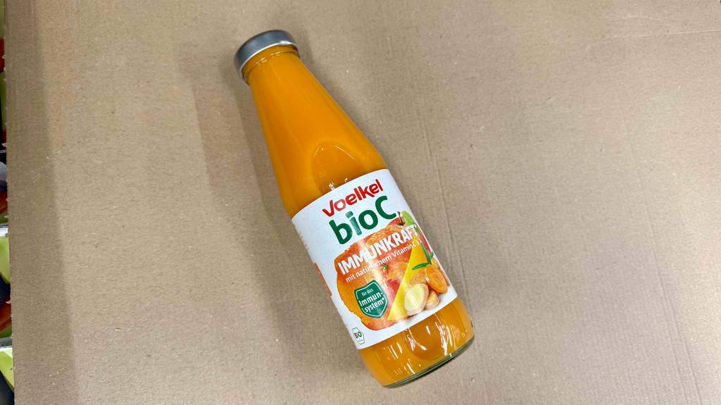 Getesteter Vitaminsaft in der Glasflasche mit Voelkel Bio C Immunkraft liegt auf einem Karton.