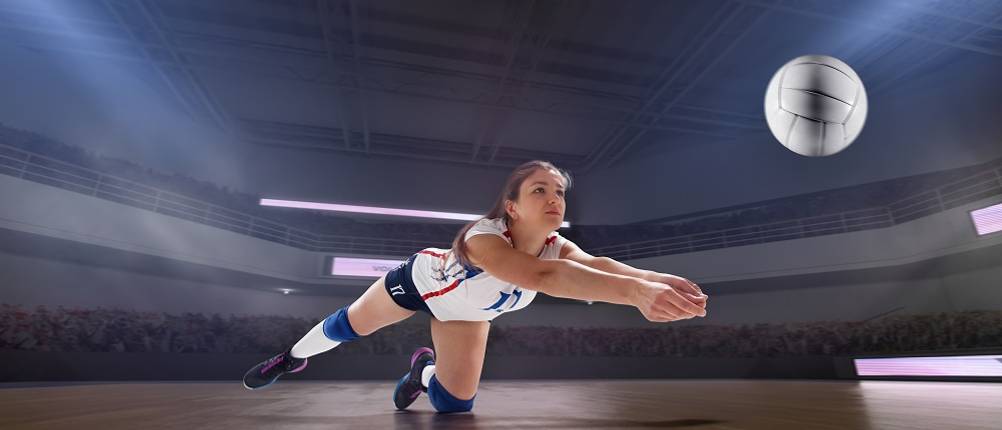 Volleyballschuhe-Damen-Test: Eine Volleyballspielerin hechtet nach einem Ball in einer Sporthalle mit Publikum