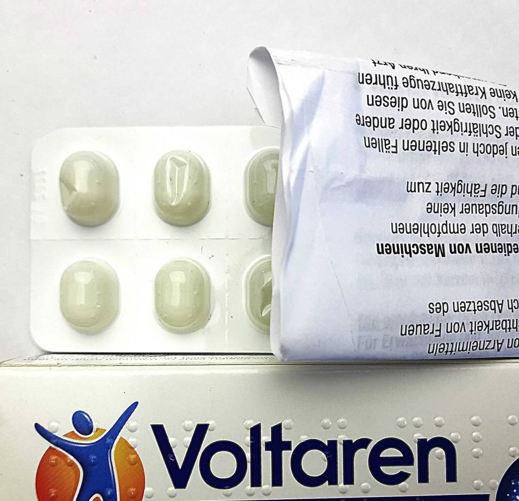 Schmerzmittel im Test. Ein weißes Blister liegt neben der Voltarenverpackung und dem Beipackzettel.