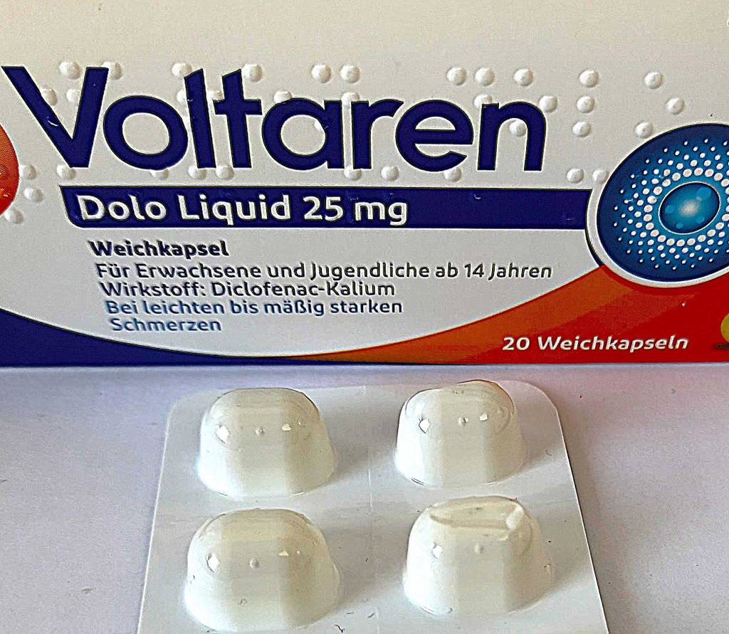 Das getestete Schmerzmittel in Weichkapseln liegt innerhalb des Blisters vor einer Packung Voltaren.