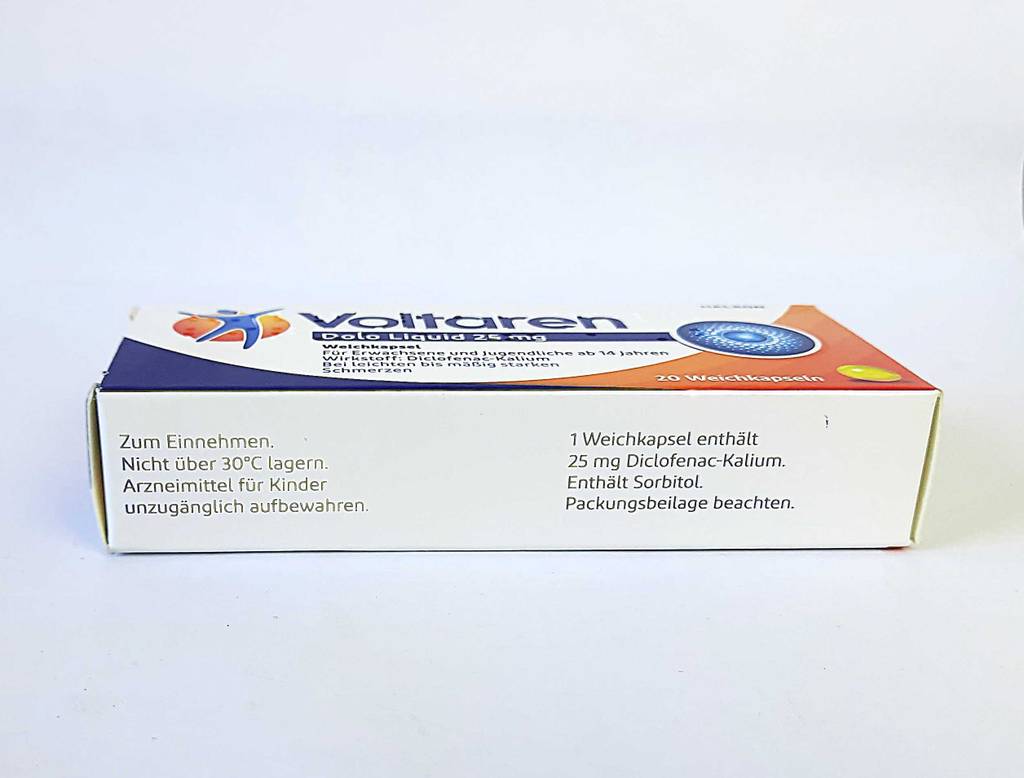 Eine Packung, auf der die Produktbeschreibung zu sehen ist, liegt mit dem getesteten Schmerzmittel von Voltaren auf einer weißen Oberfläche.