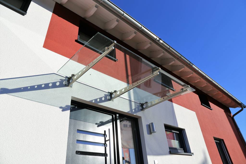Vordach im Test: Ein Vordacht aus drei Metalltraversen und Glas an einer rot-weißen Fassade über der Haustür.