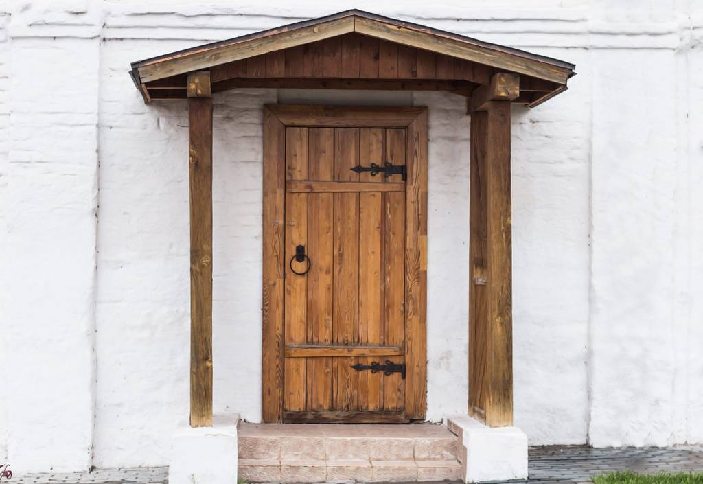 Vordach im Test: Ein rustikales Holz-Vordach vor einer ebenso rustikalen Holztür – der Stil mutet südländisch an.
