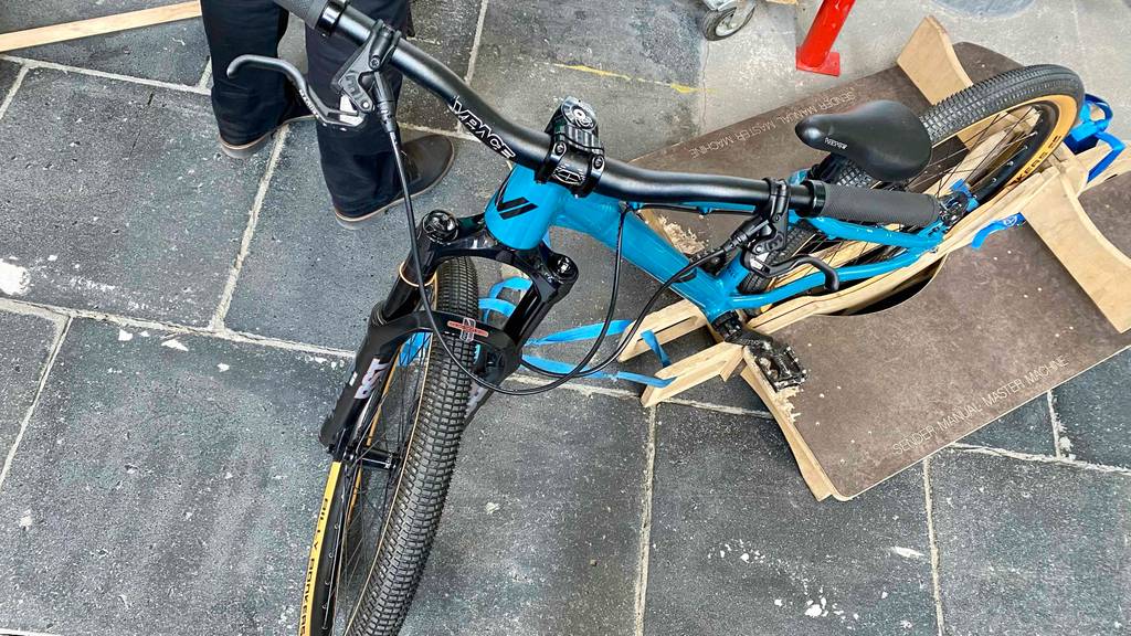 Dirtbike-Test: Ansicht von oben auf ein montiertes Dirtbike im Test, das auf grauen Steinfliesen und in einem Holz-Fahrradständer im Verkaufsbereich steht.