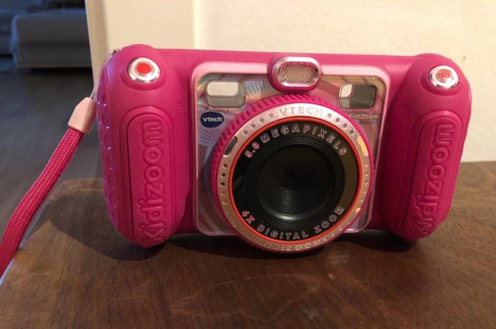 Eine rosa Kinderkamera inklusive Kidizoom steht mit Blick auf das Objektiv auf einer Holzfläche.