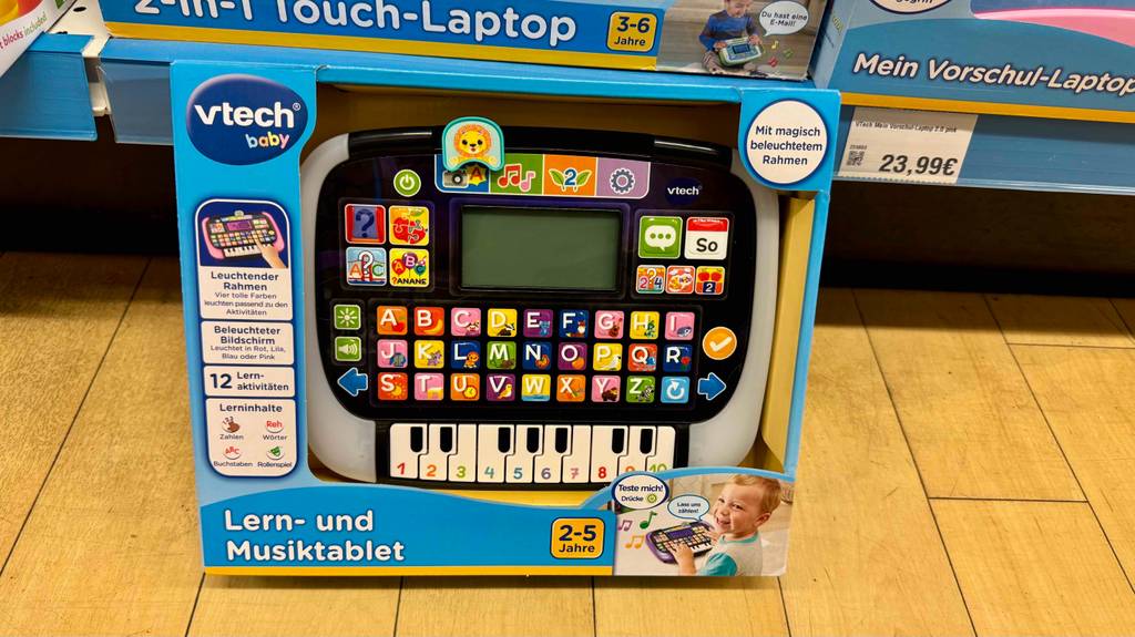 Das Lernspielzeug ab 2 Jahren im Test steht innerhalb der Verpackung mit Sichtfenster vor einem Verkaufsregal mit Kinder-Laptops.