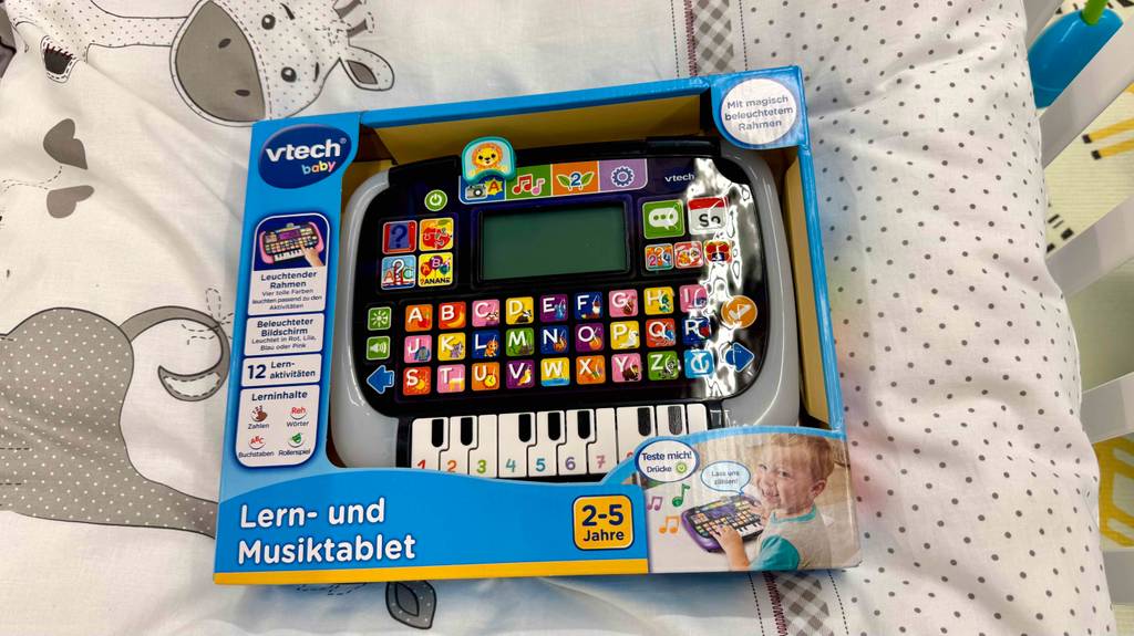 Das getestete Lernspielzeug ab 2 Jahre liegt innerhalb der Verpackung mit Sichtfenster auf einem Kinderbettbezug.