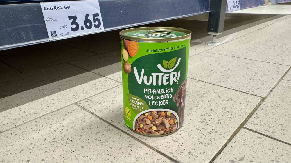 Eine Dose des getesteten veganen Hundefutters steht vor einem Regal auf dem Boden.