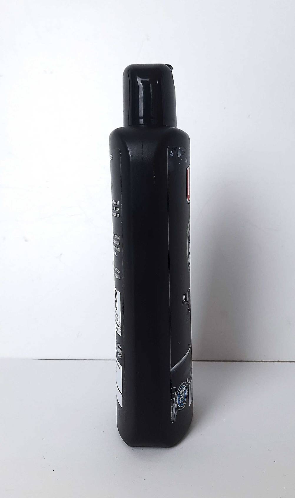 Die schwarze Kunststoffflasche mit der Autopolitur im Test steht auf einer weißen Oberfläche.