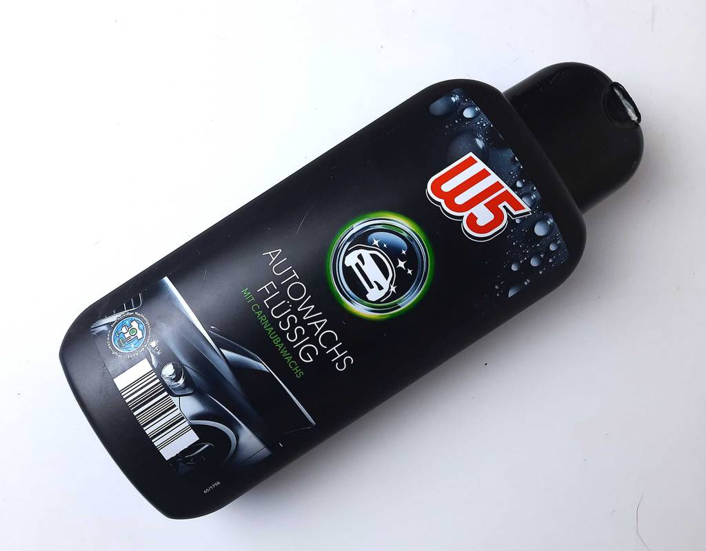 Die schwarze Kunststoffflasche mit der getesteten Autopolitur liegt geschlossen, von oben betrachtet, auf einer weißen Oberfläche.