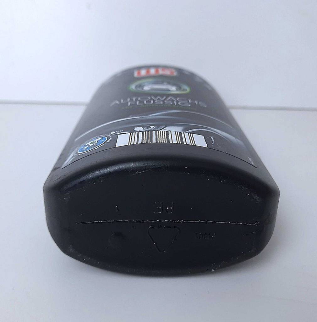 Die schwarze Kunststoffflasche mit der Autopolitur im Test liegt auf einer weißen Oberfläche.