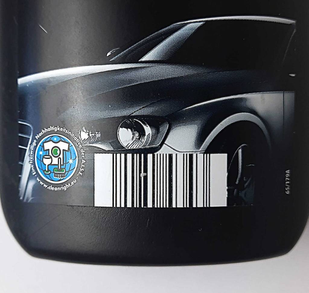 Die schwarze Kunststoffflasche mit der getesteten Autopolitur steht, mit Fokus auf das Nachhaltigkeitsetikett, auf einer weißen Oberfläche.