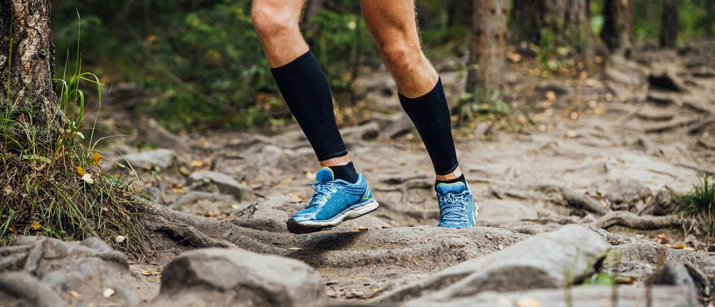 Wadenbandage-Test: Mann joggt im Wald und trägt schwarze Wadenbandagen.