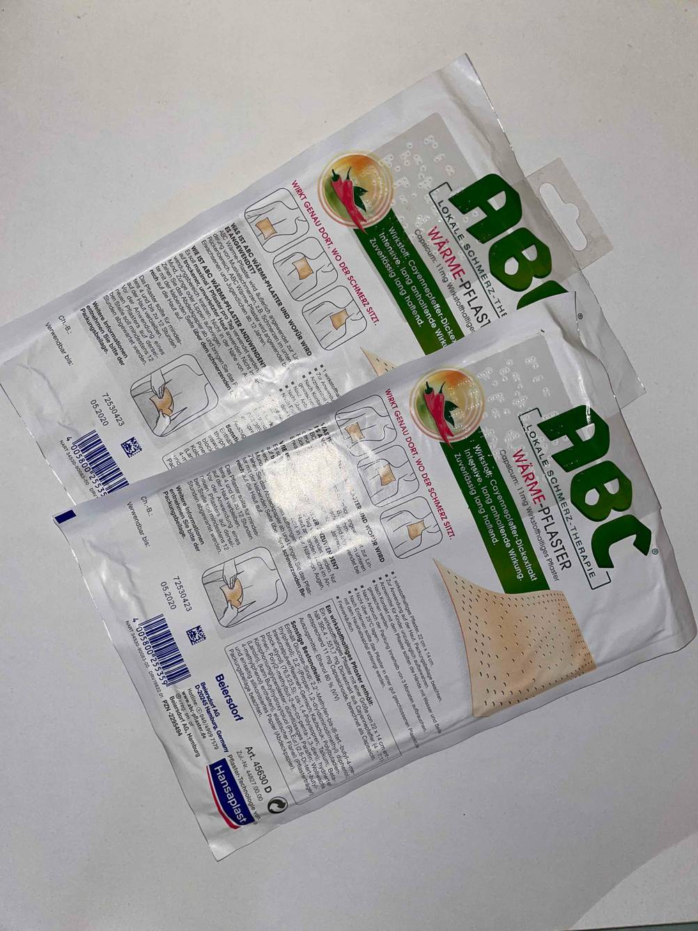 Zwei nebeneinander liegende Packungen mit der Rückseite nach oben des getesteten Wärmepflasters auf einer hellen Fläche.
