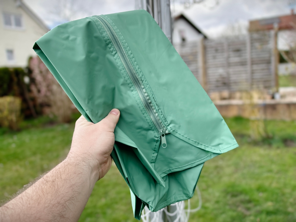 Eine grüne Schutzhaube der Brabantia Lift-O-Matic 50 wird von einer Hand im Garten gehalten.